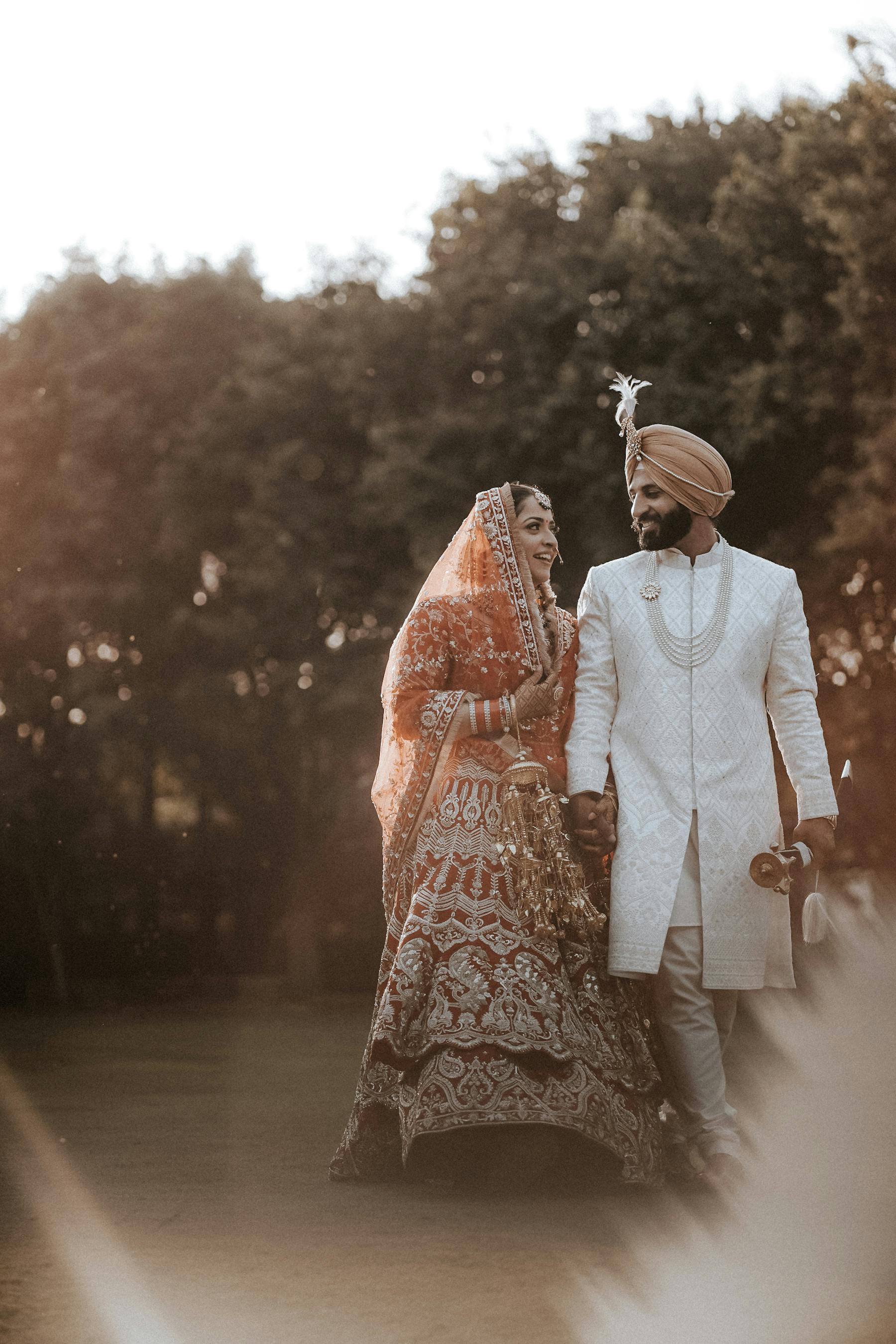 A South Asian wedding couple in traditional attire walking together at golden hour