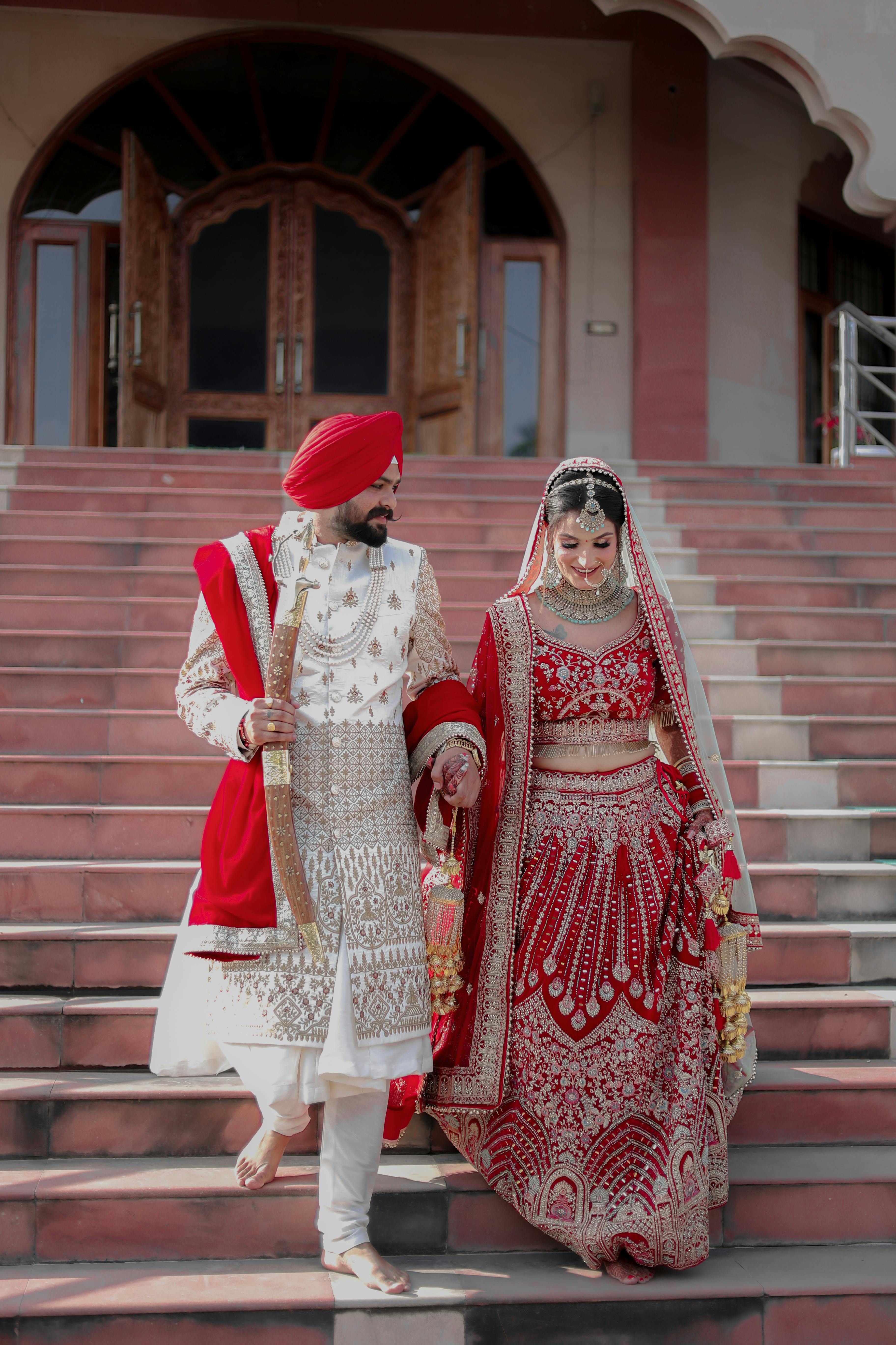 A South Asian couple in red wedding attire on temple steps